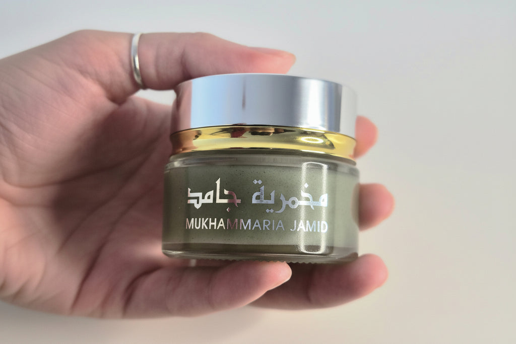 Hand holding a jar of skincare product with visible branding on a plain background